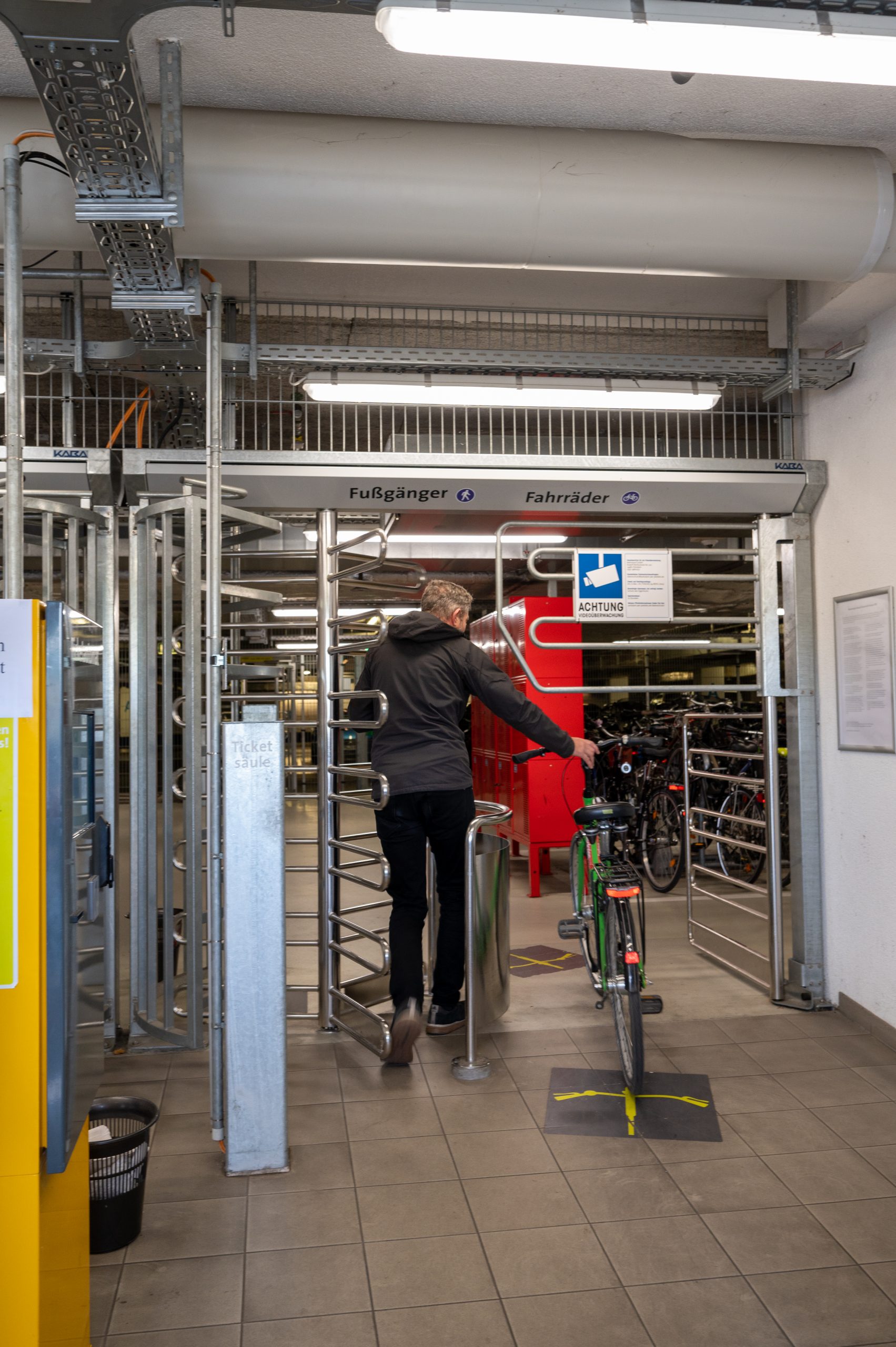 Mann schiebt sein grünes Fahrrad durch das Drehkreuz in das Fahrradparkhaus.