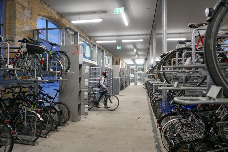 Mann schiebt Fahrrad durch Drehkreuz in das Fahrradparkhaus in Bamberg, Blick auf Doppelstockparker, die gut ausgelastet sind