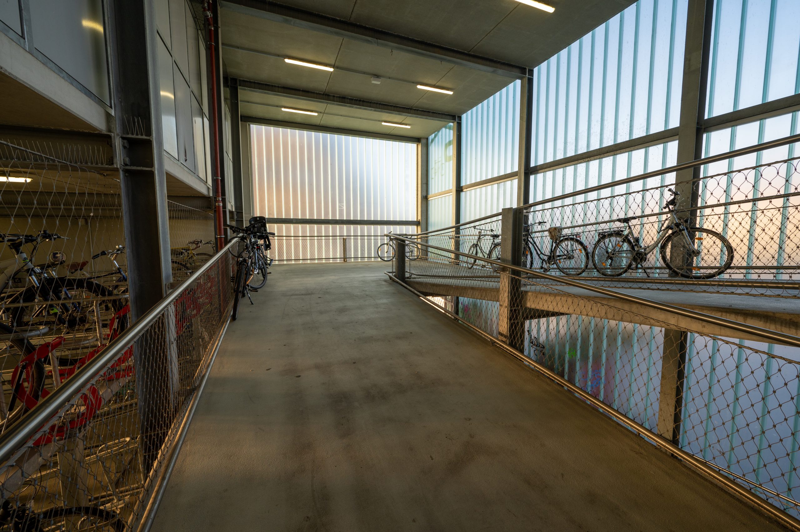 Fahrradrampe im Innern des Fahrradparkhauses aus Beton und durch das Licht, das durch die grünen Fensterscheiben fällt, sehr gut beleuchtet. 