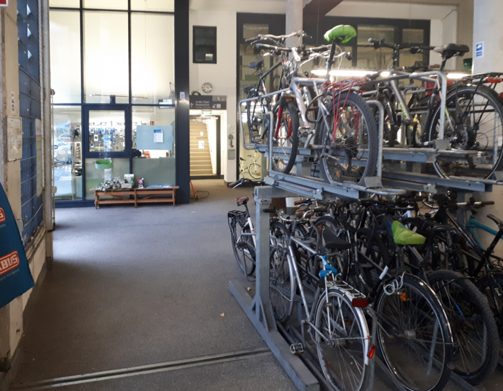 Fahrradständer in Doppeöstockparkern, im Hintergrund sieht man durch eine große Scheibe die Fahrradwerkstatt.