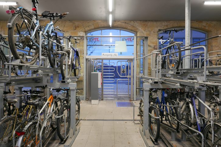 Blick auf den Ausgang des Fahrradparkhauses, das mit einem metallenen Drehkreuz verschlossen ist, darüber hängt ein Schuld, auf dem 