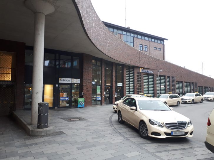 Außenansicht auf das Rondell, an dem das Radhaus liegt. Vor dem Gebäude warten Taxis.