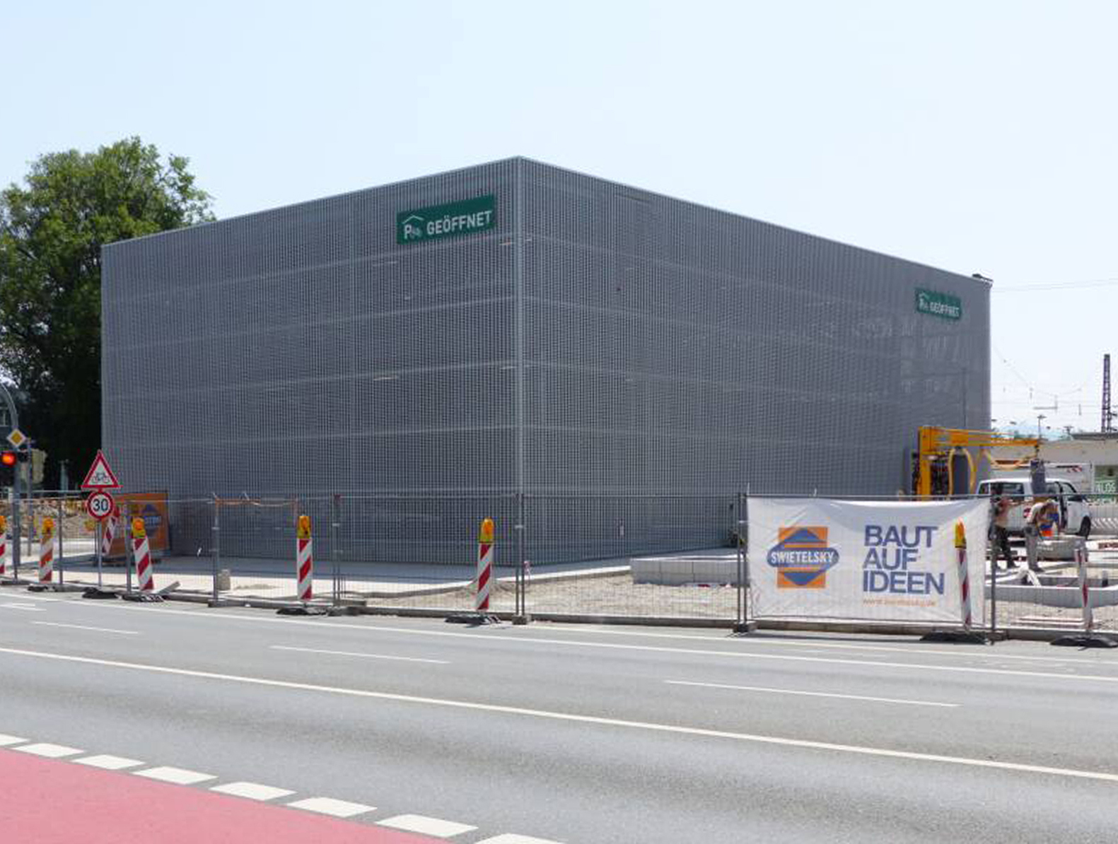 Das Fahrradparkhaus in Rosenheim ist mehrgeschossig. Ein Metall-Kubus vor einer Baustelle. 