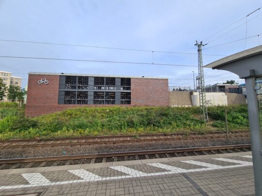 Blick von den Gleisen auf das Fahrradparkhaus, das über zwei Stockwerke reicht und in regionaltypischer Ziegelbauweise entworfen wurde.