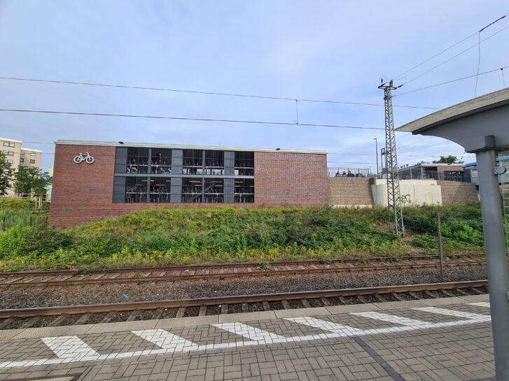 Blick von den Gleisen auf das Fahrradparkhaus, das über zwei Stockwerke reicht und in regionaltypischer Ziegelbauweise entworfen wurde.