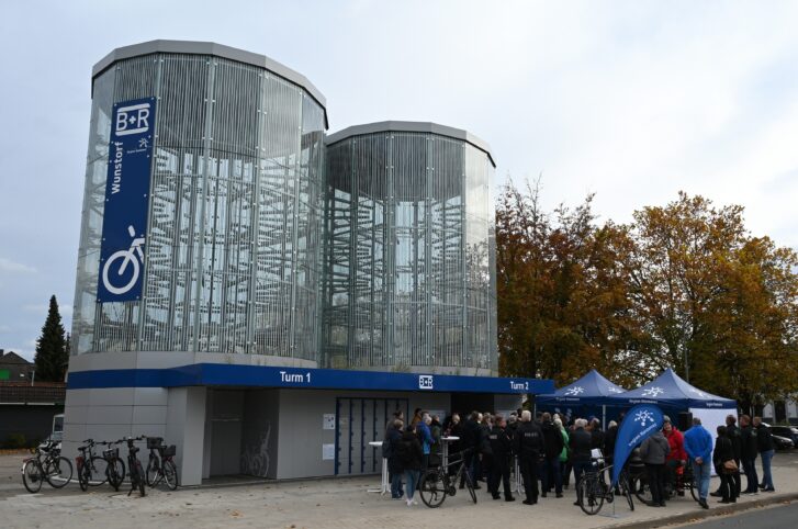 Eröffnungsfeier der Bike Tower. Menschen stehen an Stehtischen vor den automatischen Fahrradparktürmen. 