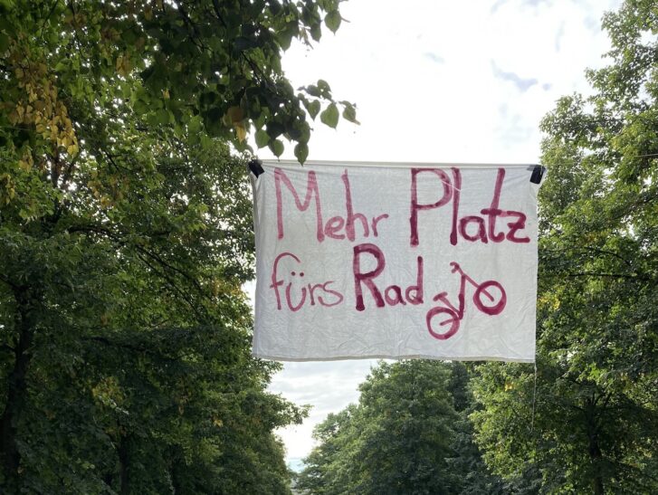 Banner hängt zwischen Bäumen mit Aufschrift „Mehr Platz fürs Rad“